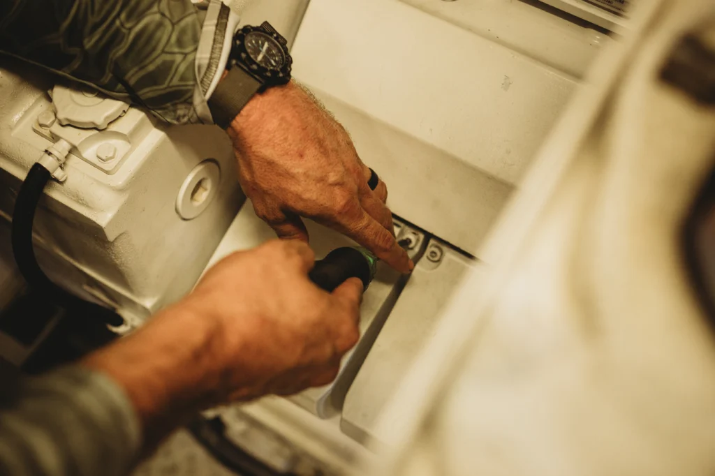 Image of Marcus Shubert, Master Marine Mechanic, repairing a piece of equipment in the engine compartment of a boat.